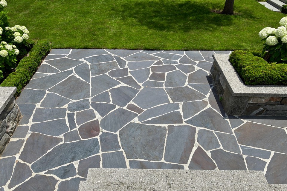 A natural flagstone patio meeting granite steps beside a lawn.